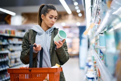 Young woman reading nutrition label and ingredients while buying dairy product in a supermarket; treatments for lactose intolerance concept